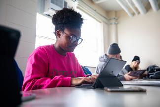 A female student sitting in a classroom working on an iPad.