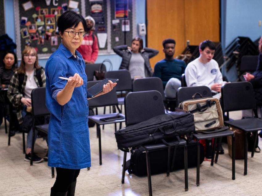 An instructor stands in front of a classroom holding an iPad.